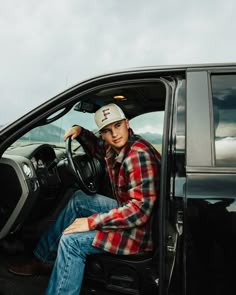 a young man sitting in the driver's seat of a black truck with his hand on the steering wheel