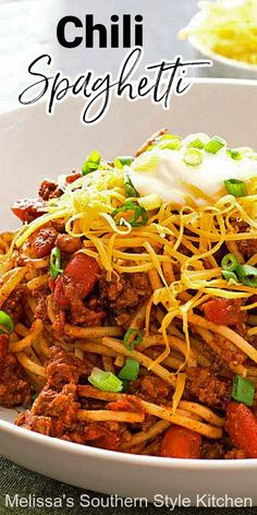 chili spaghetti in a white bowl with sour cream on top and green onions around the edges