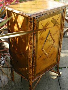 an old wooden cabinet with dragonflies painted on the front and sides, sitting next to some plants