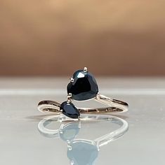 two pear shaped black diamond rings sitting on top of a white surface with reflections in the water