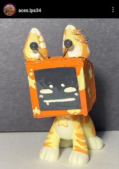 an orange and white toy with a black board on it's face, sitting in front of a gray background