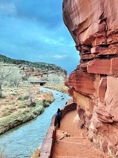 two people standing on the side of a cliff next to a river