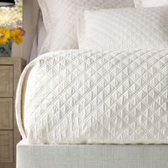 a close up of a bed with white linens and flowers on the nightstand next to it