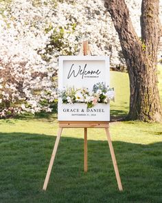 an easel with a welcome sign on it in front of some trees and grass