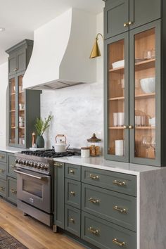 a kitchen with green cabinets and marble counter tops, gold pulls on the oven hood