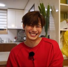 a man in a red shirt is smiling at the camera while standing next to a kitchen counter