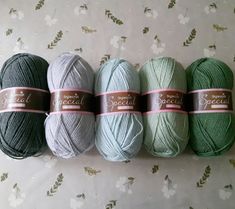 four skeins of yarn are lined up on a floral wallpapered surface