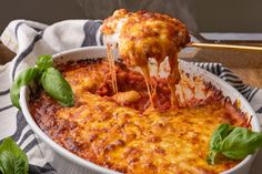 a slice of lasagna being lifted from a casserole dish with basil leaves