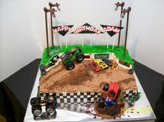 a birthday cake made to look like a dirt track with monster trucks and flags on top