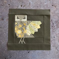 a patchwork bird sitting on top of a piece of fabric