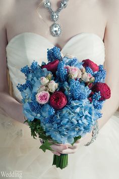 a bride holding a bouquet of blue and pink flowers in her hands with a diamond necklace on her neck