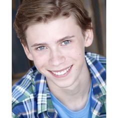 a young man smiling at the camera wearing a blue and green plaid shirt with his hair pulled back