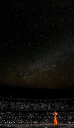 a woman in an orange dress stands on stage under the night sky with stars above her