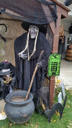 a creepy scarecrow dressed in black holding a broom next to a potted witch