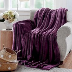 a purple blanket sitting on top of a couch next to a white vase with flowers