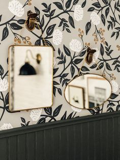 two mirrors are hanging on the wall next to a black and white flowered wallpaper