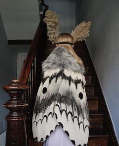 a woman walking down the stairs with a large moth on her back