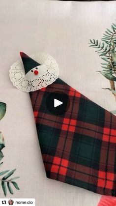 a red and black plaid pillow on top of a white table cloth with an ornament in the shape of a cat