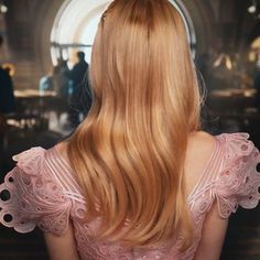 the back of a woman's head with long blonde hair in a pink dress