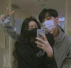 a man and woman wearing face masks taking a selfie with their cell phones in front of them