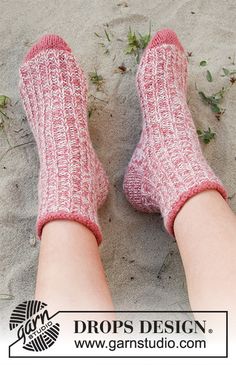 a woman's feet in pink socks on the sand with grass growing behind her