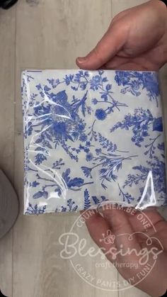 someone is holding up a blue and white floral gift bag with clear plastic wrapping on it