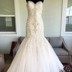 a wedding dress is displayed on a mannequin in front of a couch and chair