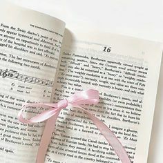 an open book with a pink ribbon on top of it and music notes in the pages