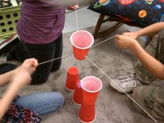 three children are sitting on the floor playing with plastic cups and string strung to match them