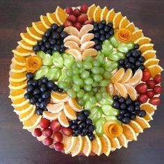 a fruit platter with grapes, oranges, and other fruits arranged in the shape of a flower