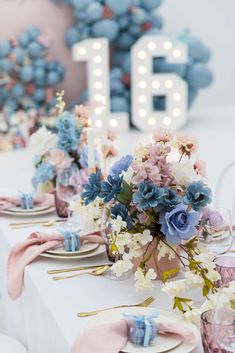 the table is set with blue and pink flowers in vases, napkins, and plates