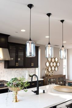 a kitchen with black cabinets and lights hanging from it's ceiling above the island