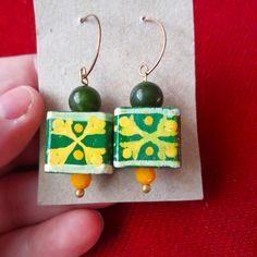 a pair of earrings with green and yellow designs on them sitting on top of a piece of paper