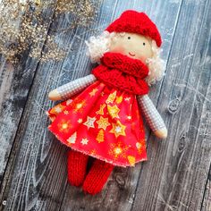 a red knitted doll laying on top of a wooden floor next to dried flowers