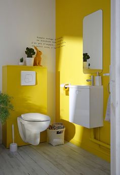 a white toilet sitting next to a yellow wall and potted plant on top of it