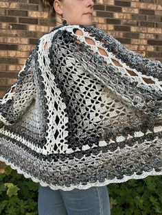 a woman is wearing a crocheted shawl in front of a brick wall