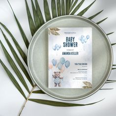 a baby shower card on top of a metal plate with palm leaves next to it