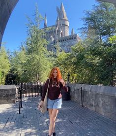 a woman with red hair is walking down the sidewalk in front of hogwart's castle