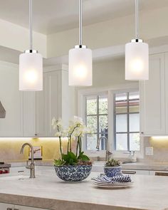 three lights hanging over a kitchen island with flowers in the bowl and plates on the counter