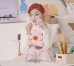 a woman sitting at a desk holding a pink stuffed animal in front of her face