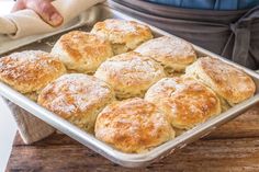 a pan filled with biscuits on top of a wooden table next to a person holding a towel