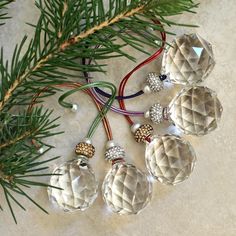 four glass ornaments hanging from a tree branch on a marble surface with christmas decorations in the background