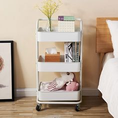 a white cart with books and stuffed animals on it next to a bed in a bedroom