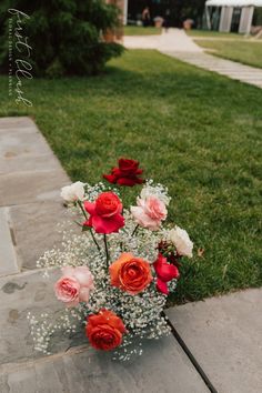 a vase filled with red and white flowers sitting on top of a cement slab next to grass