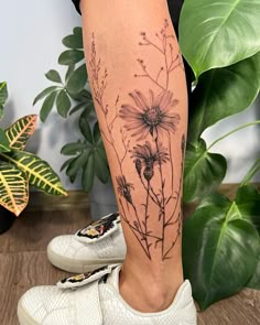 a woman's leg with a flower tattoo on it, next to a potted plant