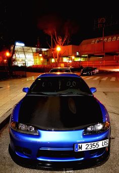 a blue sports car parked on the side of the road at night with its lights on