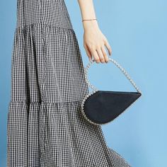 a woman is holding a black and white handbag in her right hand while standing against a blue background