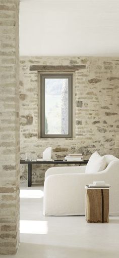 a living room filled with furniture next to a window and a white couch in front of a stone wall