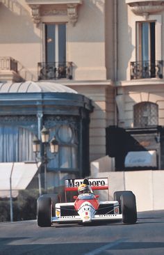 a man driving a race car down a street in front of a tall white building