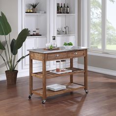 a kitchen island cart with marble top in front of a window and potted plant